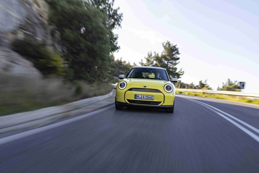 The all-electric MINI Cooper E in Sunny Side Yellow features white roof and mirror caps, 17″ U-Spoke rims, and a sporty interior, perfectly matching Greece's Mediterranean charm.