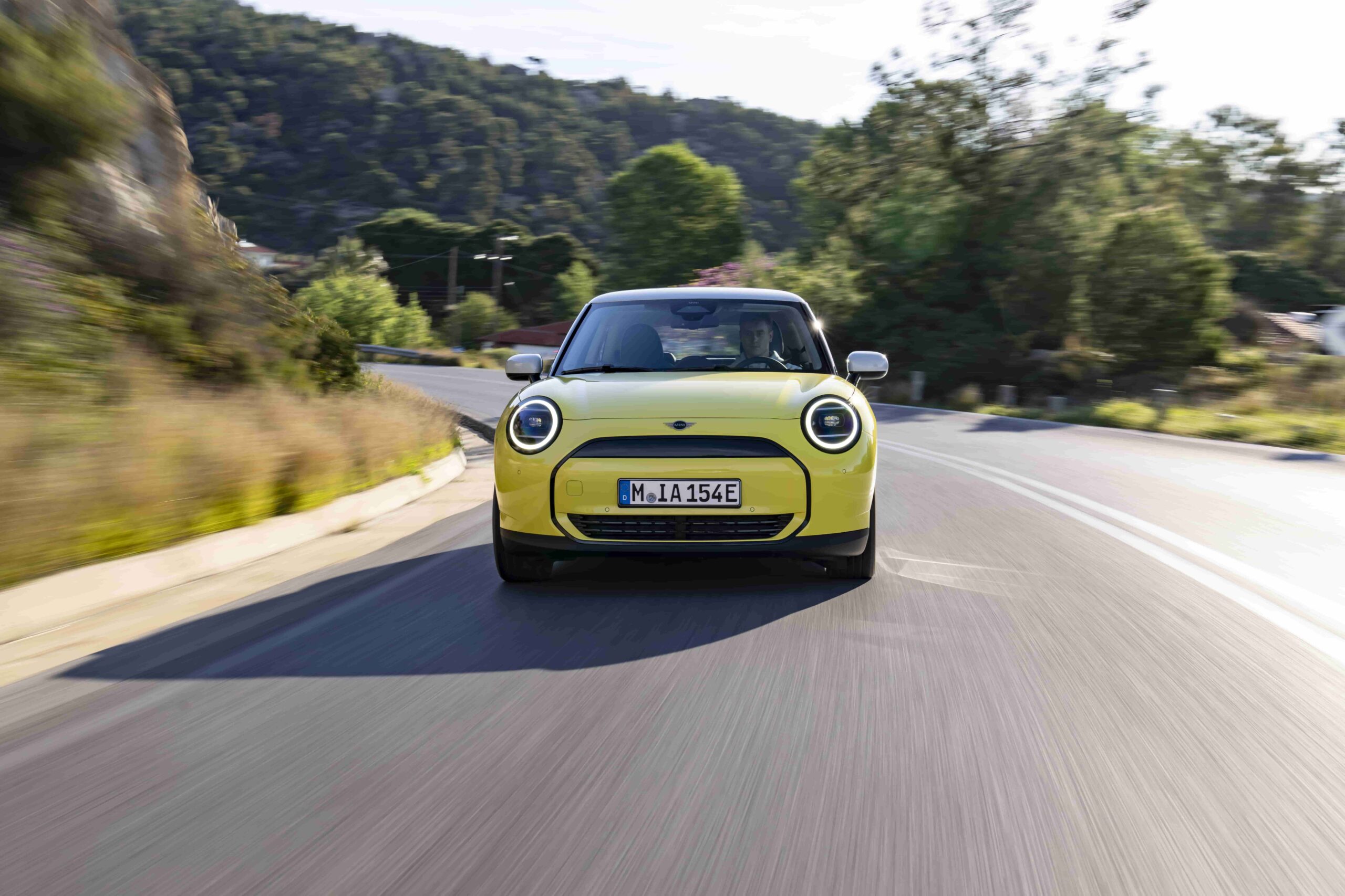 The all-electric MINI Cooper E in Sunny Side Yellow features white roof and mirror caps, 17″ U-Spoke rims, and a sporty interior, perfectly matching Greece's Mediterranean charm.